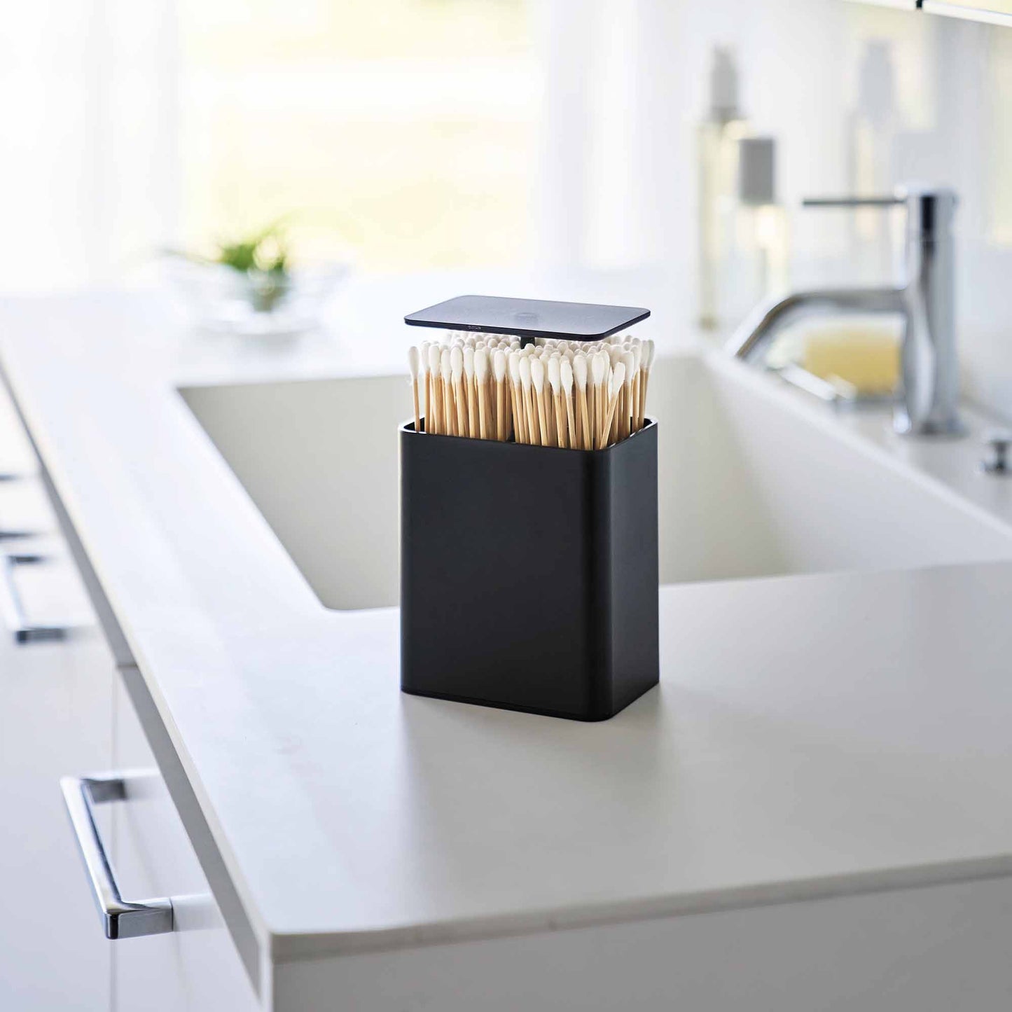 Black Cotton Swab push-top case on a modern bathroom counter. QTips shown in the case.