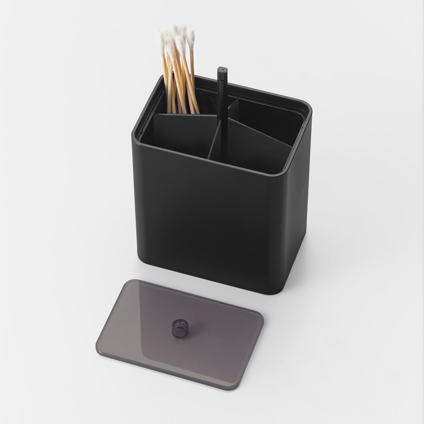 Cotton Swab Push-Top Case in black from Yamazaki Home with Qtips in one of 4 compartments. The semi-transulsent cap is popped off for easy refilling.