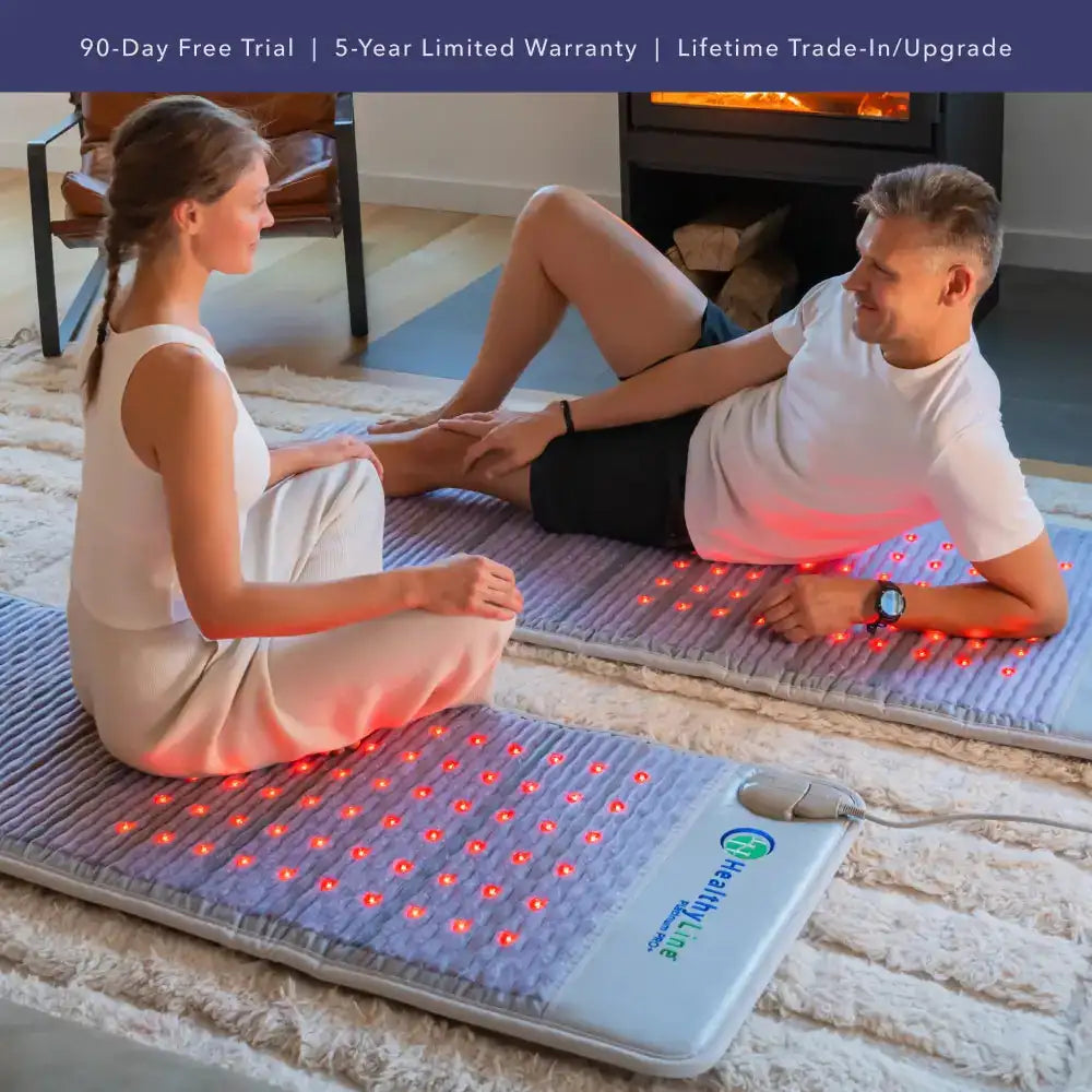 Couple relaxing on dual HealthyLine PEMF infrared heating mats with red LEDs in cozy living room