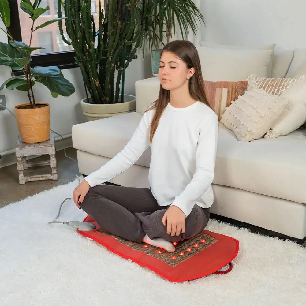 Woman using red HealthyLine PEMF infrared heating mat with LED lights for relaxation