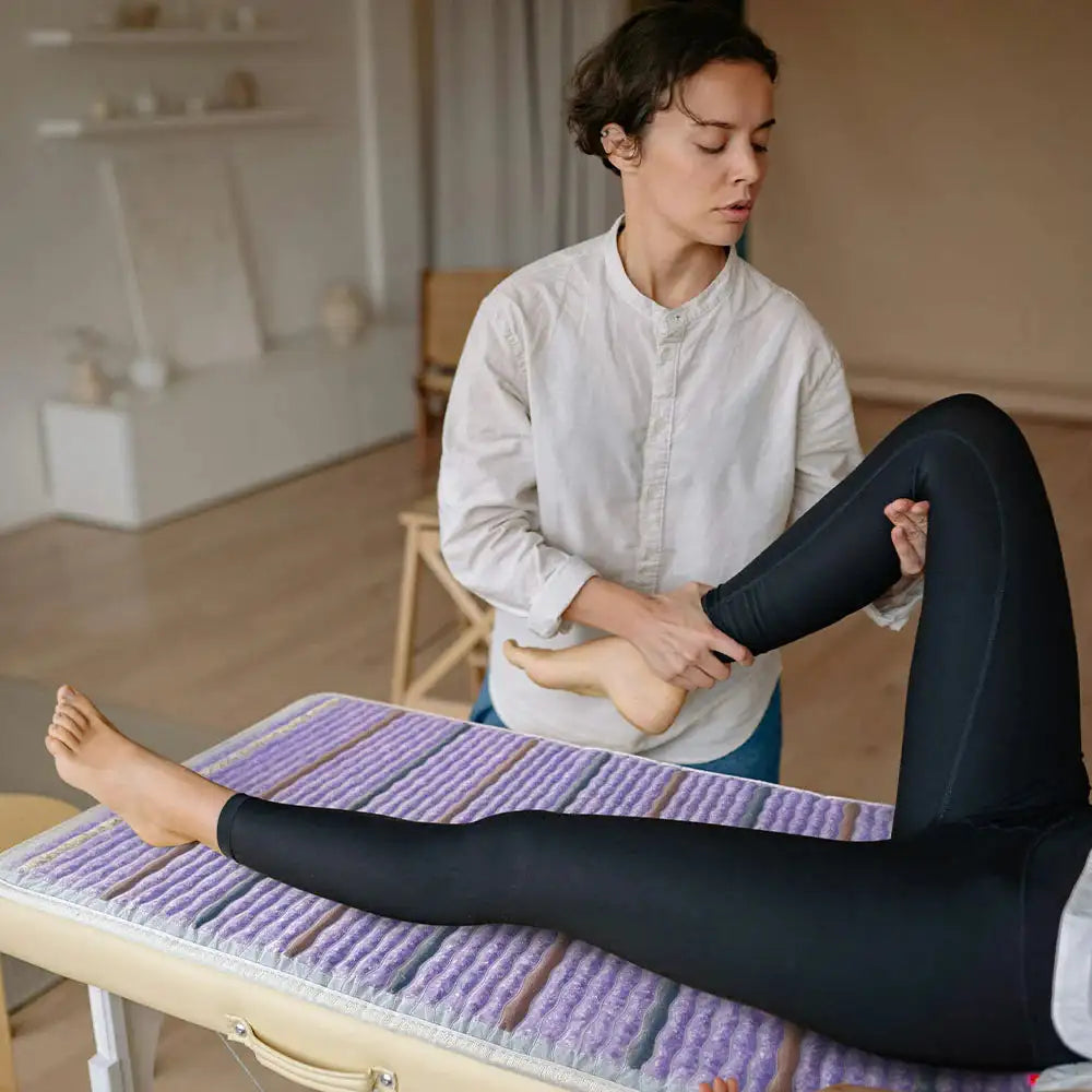 Therapist stretching client leg on HealthyLine PEMF infrared therapeutic mat in spa setting