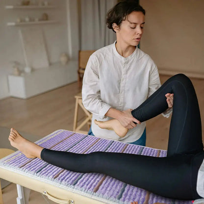 Therapist stretching client leg on HealthyLine PEMF infrared therapeutic mat in spa setting