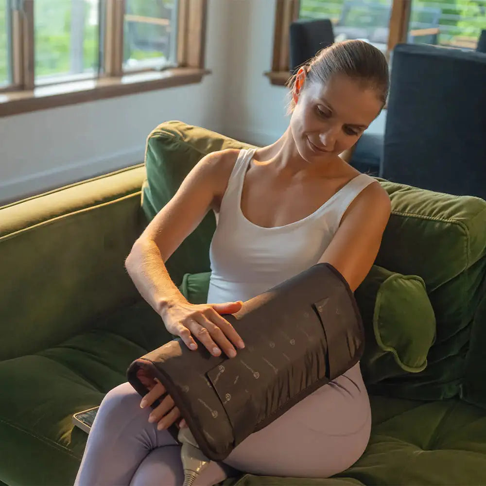 Woman applying heated arm sleeve over lavender leggings for targeted muscle recovery