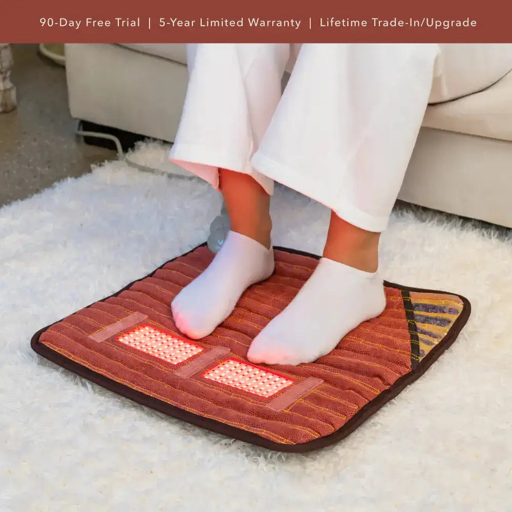 Person standing barefoot on orange infrared heating mat with red LED therapy lights