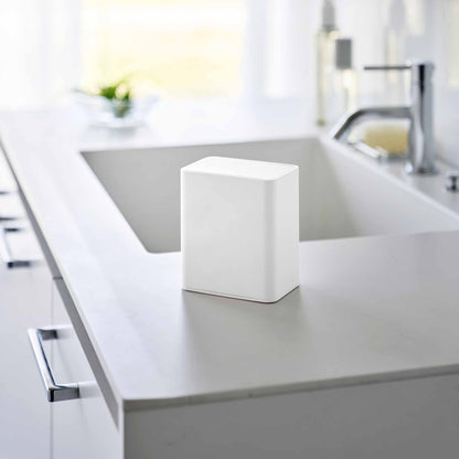 White cotton swab push-top case shown with the lid pushed down, concealing interior storage on a modern bathroom countertop.