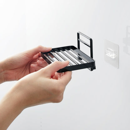 Hands installing Yamazaki Home's black Traceless Adhesive Soap Tray on a bathroom wall, demonstrating its ease of use.