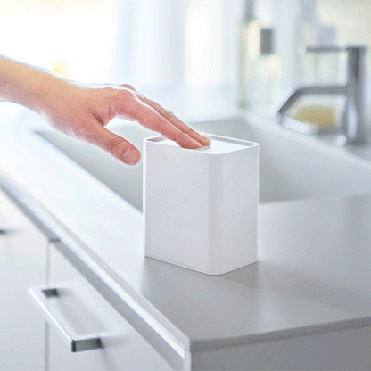 Hand pushes White cotton swab push-top case down, concealing interior Qtip storage in a minimalist bathroom.