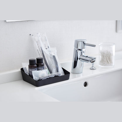 Medium black Accessory Tray holding beauty products on bathroom sink counter by Yamazaki Home.