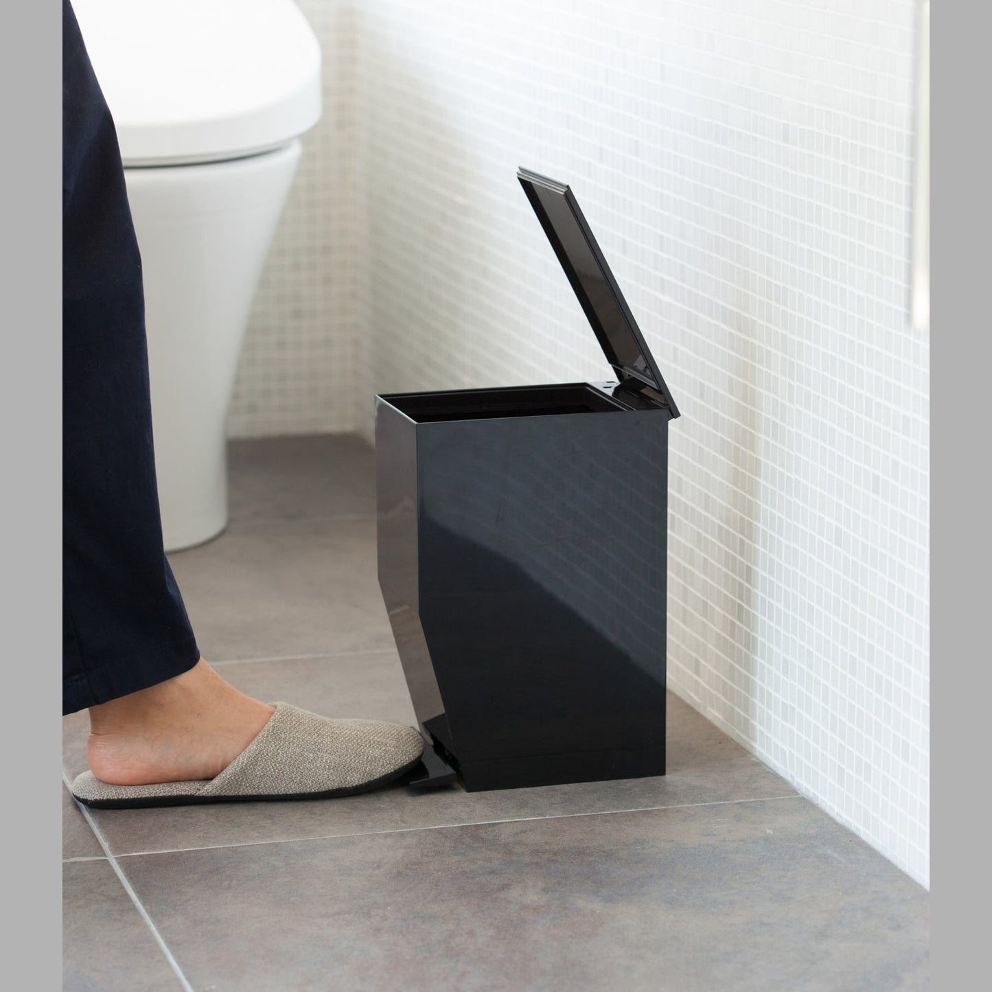 Side view of black Step Trash Can open in bathroom by Yamazaki Home.