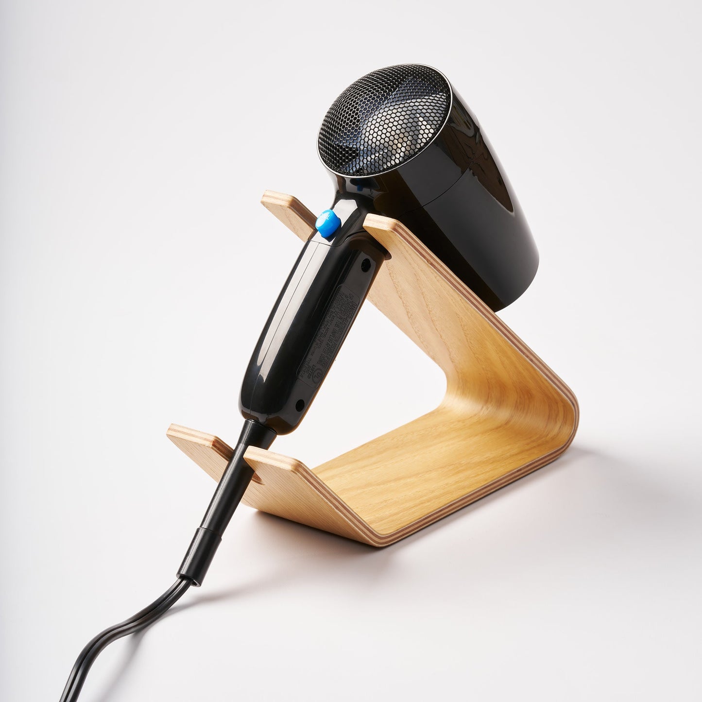 Hair Dryer and Iron Stand - Wood in Ash by Yamazaki Home holding a black hair dryer with a white background.