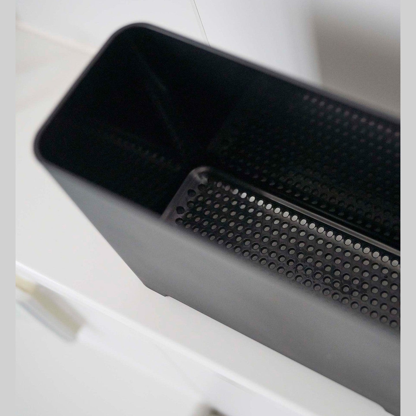 Close up of draining holes of black Yamazaki Self-Draining Bathroom Organizer
