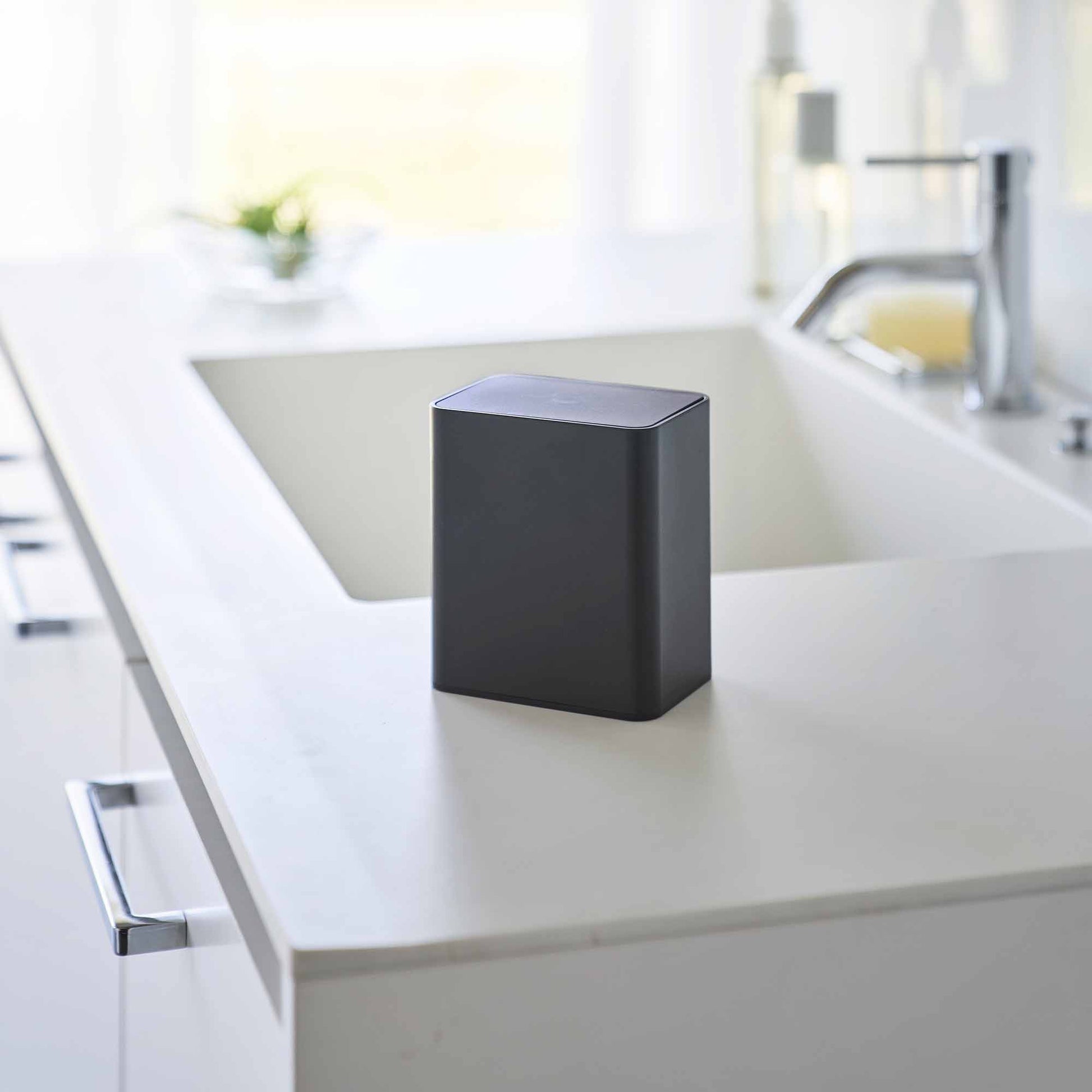 Black cotton swab push-top case shown with the lid pushed down, concealing interior storage on a modern bathroom countertop.