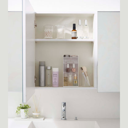 A white medicine cabinet is open to display the inside contents. Sunlight is focused on the right upper corner. Below is a bathroom sink.