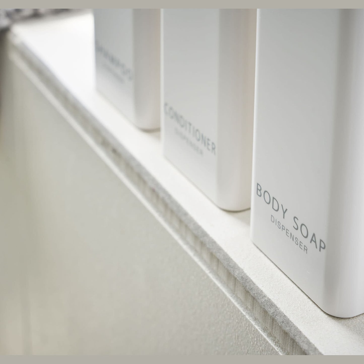 Close up bottom view of Yamazaki Home white Shampoo, Conditioner, and Body Soap dispensers.