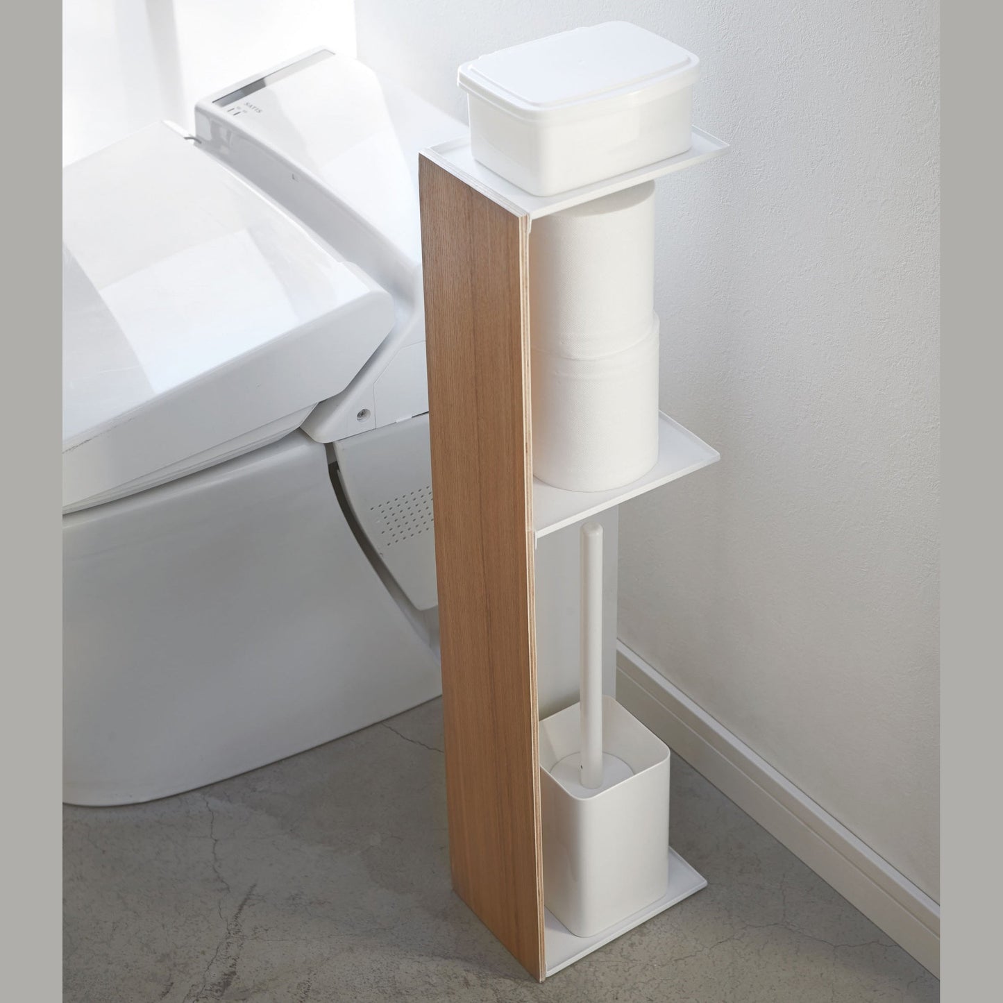 Toilet Paper Stocker holding wet wipes, toilet paper, and toilet brush in bathroom by Yamazaki Home.