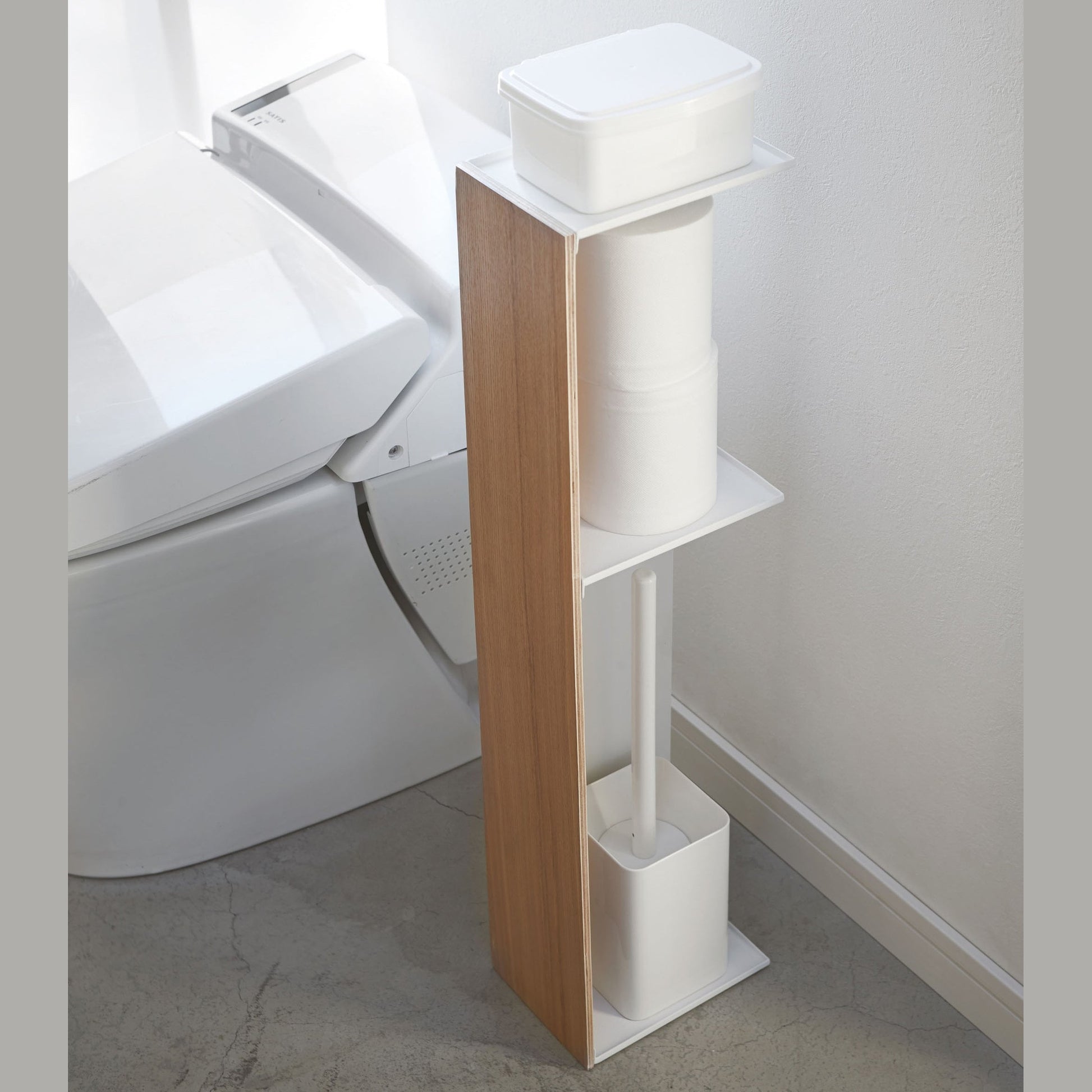 Toilet Paper Stocker holding wet wipes, toilet paper, and toilet brush in bathroom by Yamazaki Home.