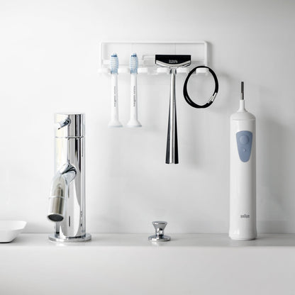 Yamazaki Home's white Traceless Adhesive Toothbrush Holder on a bathroom wall, holding two toothbrushes and a razor beside a faucet.