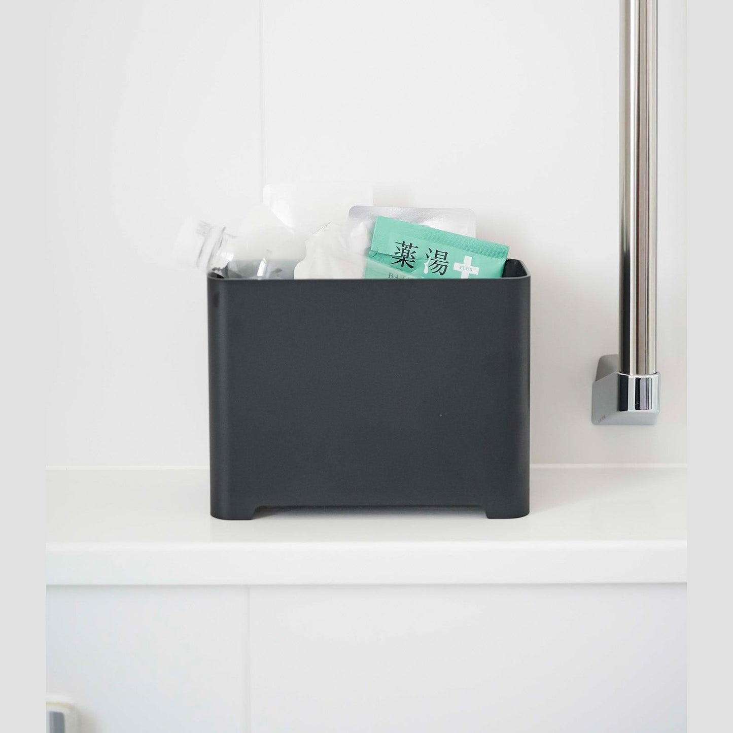 Frontal view of black Yamazaki Self-Draining Bathroom Organizer filled with bath supplies