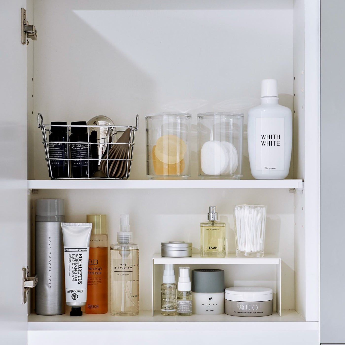 Open medicine cabinet showing white countertop riser on bottom shelf. Upper level of the riser holds perfume and hair products, while skincare and small sprays are stored on the bottom.