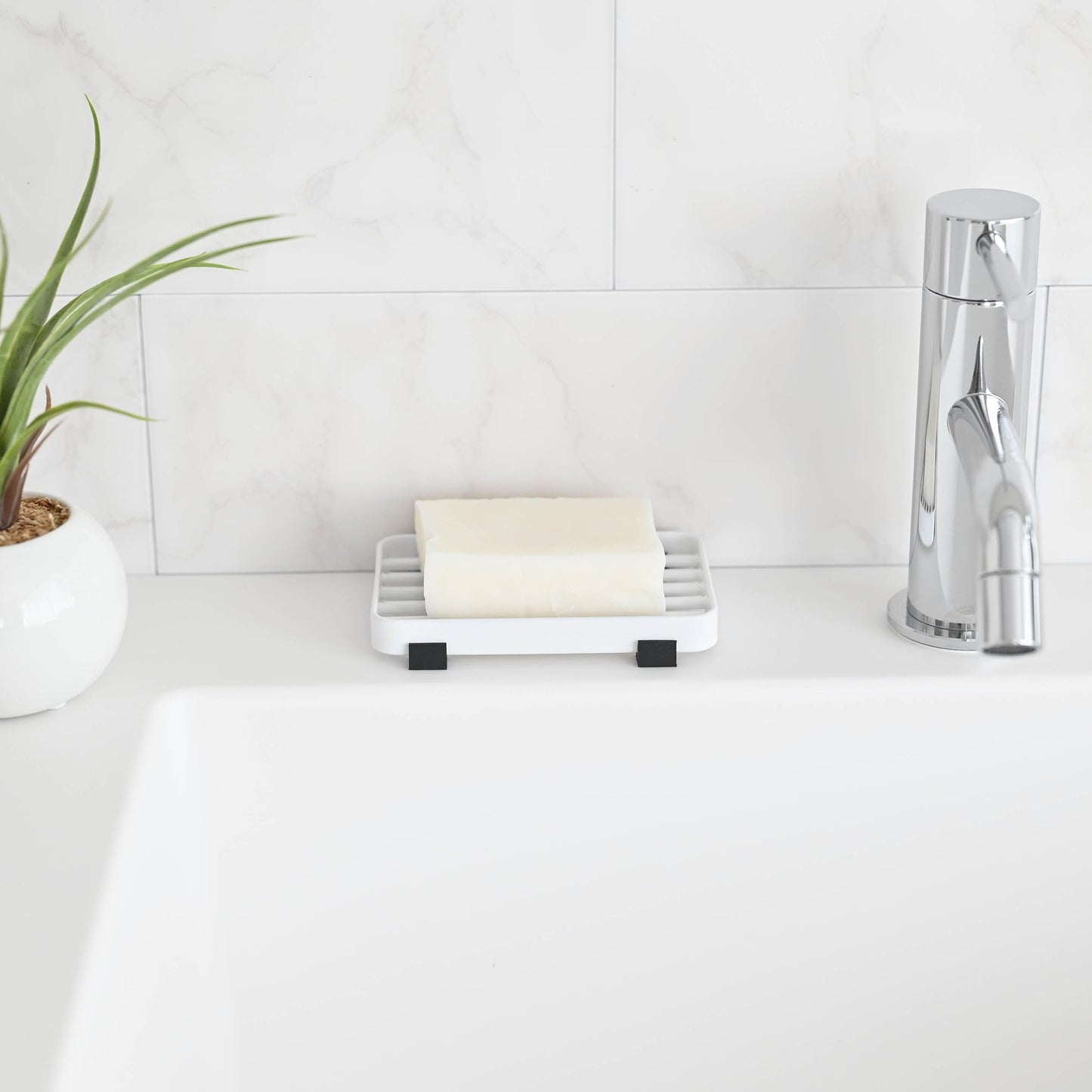 Front view of White Slotted Soap Tray holding soap bar on bathroom countertop by Yamazaki Home.