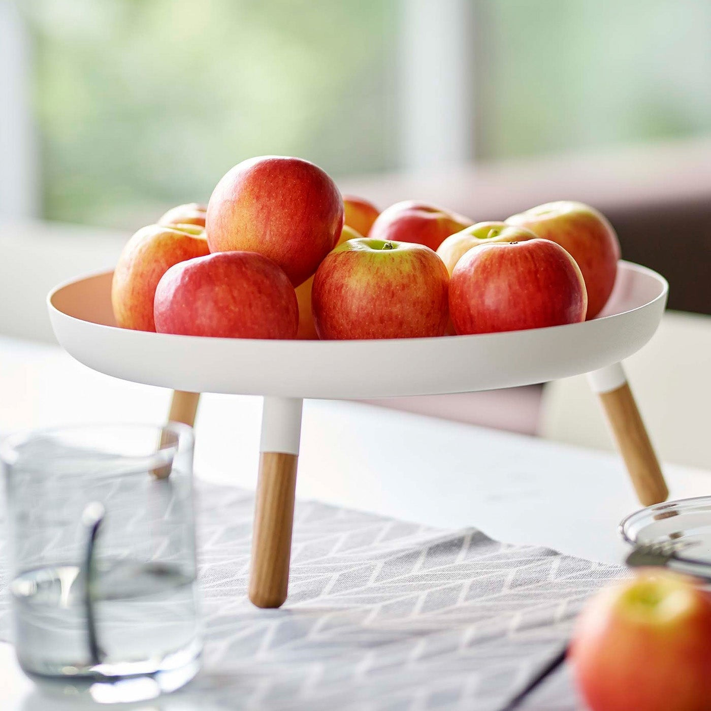Close up of white Yamazaki Countertop Pedestal Tray with apples on top on a dining table