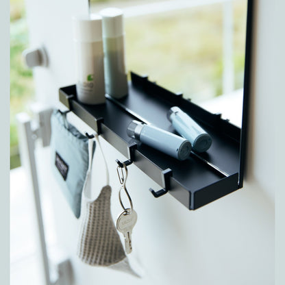 A close up of a black Yamazaki Magnetic Mirror With Storage Rack attached to a door with a hanging bag, mask, and key.