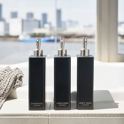 Front view of Yamazaki Home black Shampoo, Conditioner, and Body Soap dispensers on the ledge of a modern bathtub.