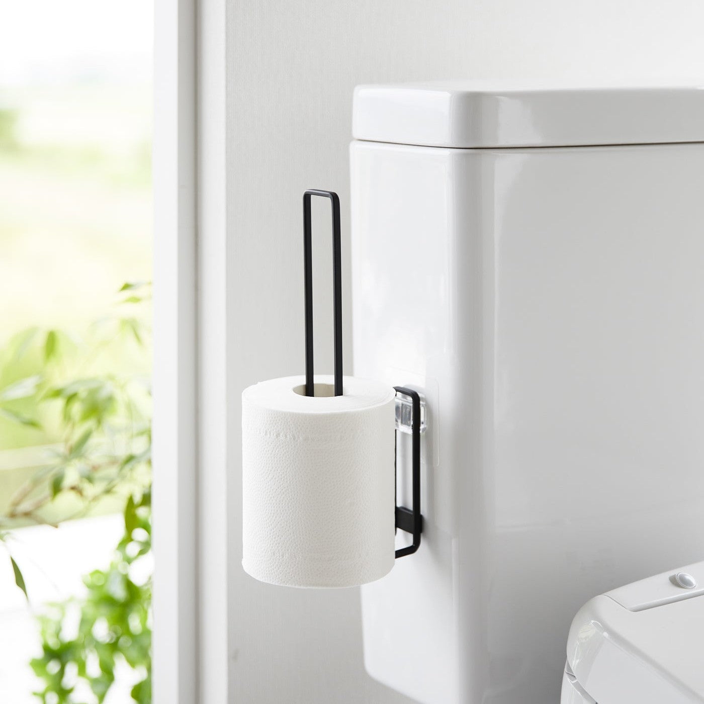 One toilet paper roll stored on a black Yamazaki Home Traceless Adhesive Toilet Paper Holder attached to a toilet