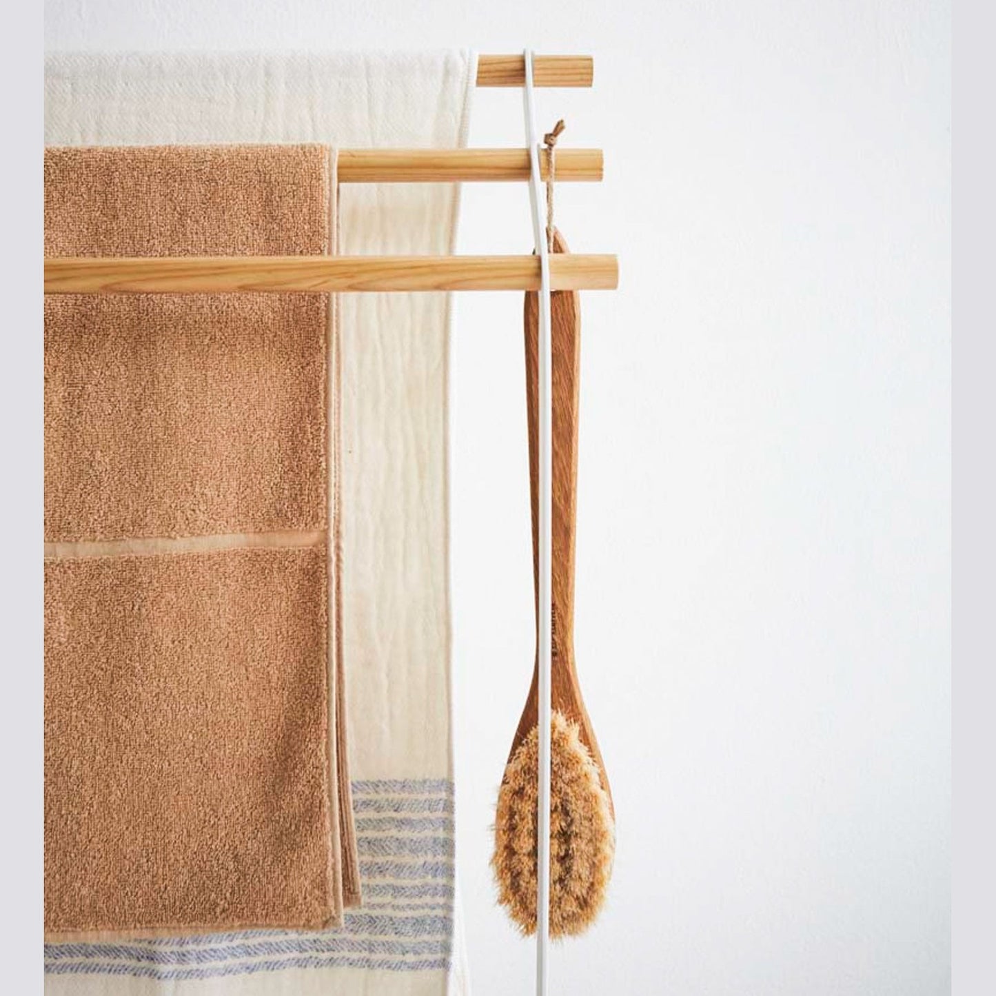 Front view of Bath Towel Rack holding towels and brush on white background by Yamazaki Home.