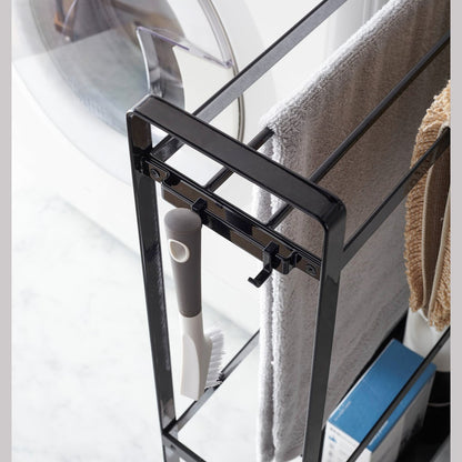 Close up corner view of black Rolling Towel Rack holding towel, mat, and cleaning items in laundry room by Yamazaki Home.