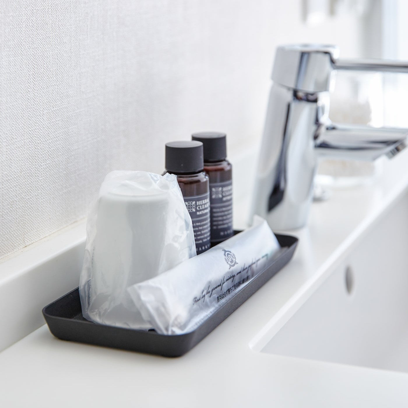 Side view of flat black Accessory Tray holding cup, soap, and toothbrush on bathroom sink counter by Yamazaki Home.