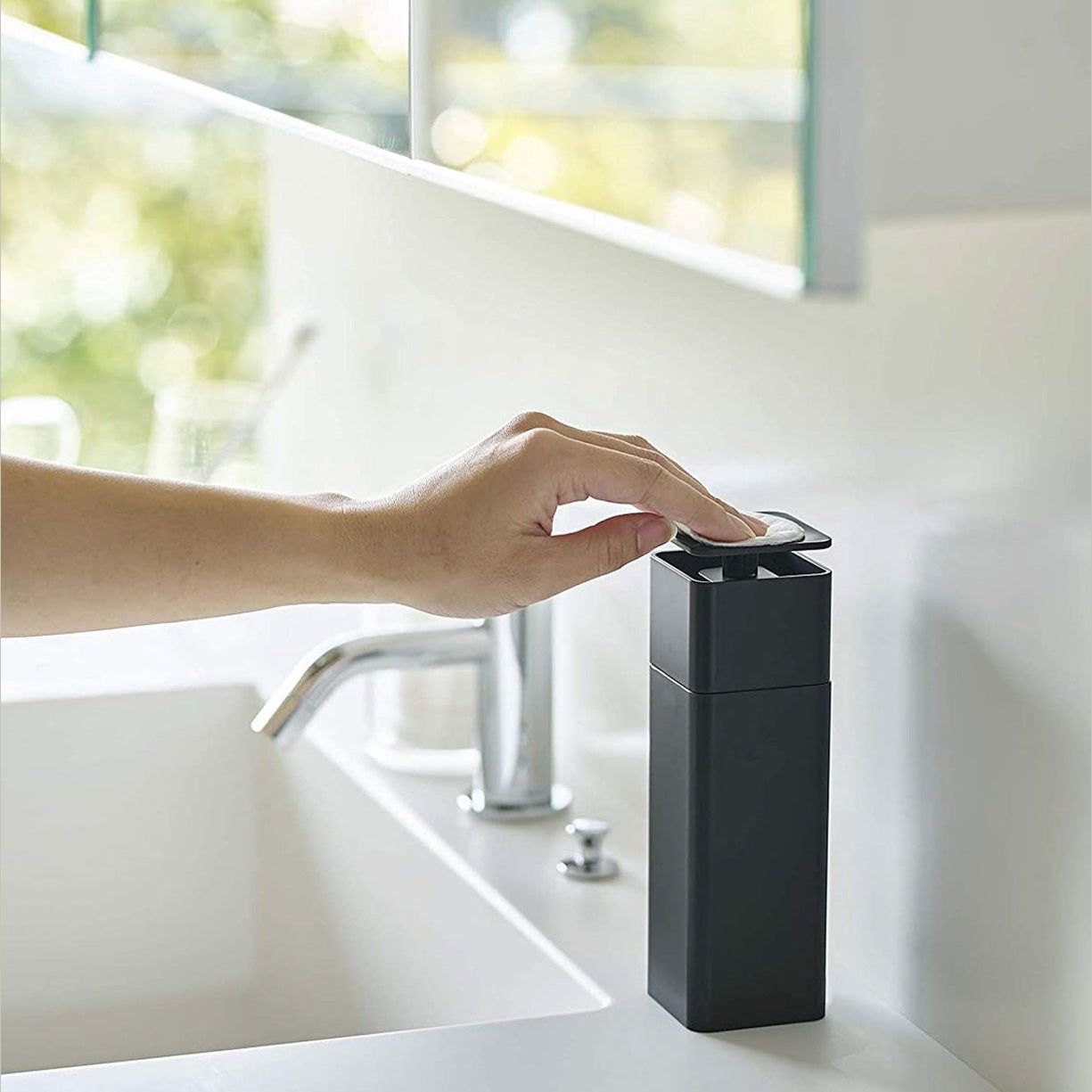 Side view of black One-Handed Push Soap Dispenser on bathroom sink countertop by Yamazaki Home.