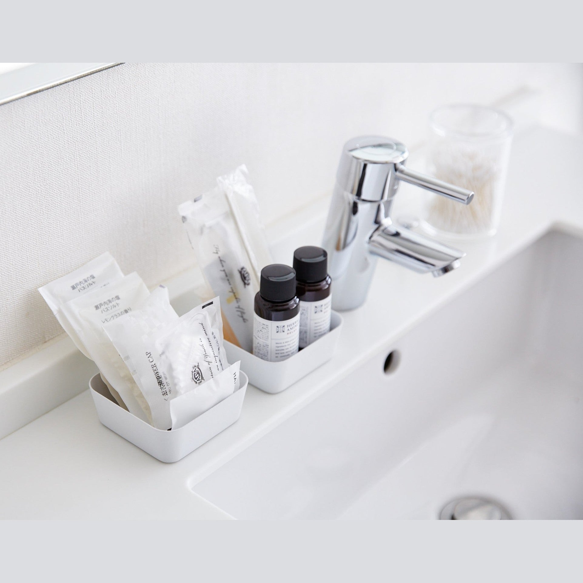Small white Accessory Trays holding beauty items on bathroom sink counter by Yamazaki Home.
