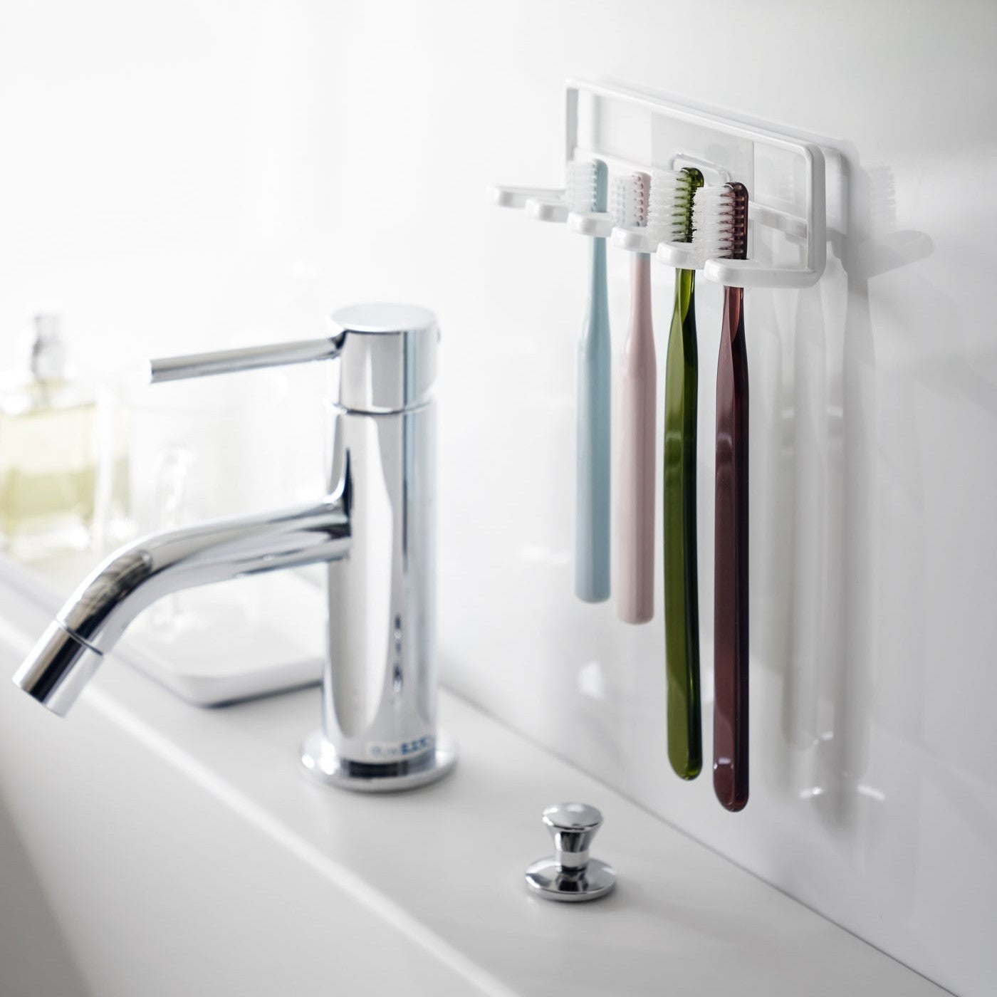 Yamazaki Home's Traceless Adhesive Toothbrush Holder, white, mounted on a bathroom wall with four colorful toothbrushes and a chrome faucet.