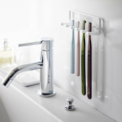 Yamazaki Home's Traceless Adhesive Toothbrush Holder, white, mounted on a bathroom wall with four colorful toothbrushes and a chrome faucet.