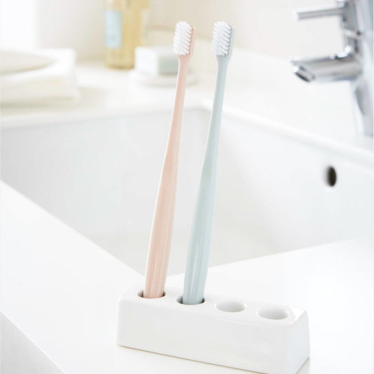 Front Ceramic Toothbrush Stand holding toothbrushes on bathroom counter by Yamazaki Home.