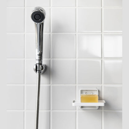 Yamazaki Home's white Traceless Adhesive Soap Tray in a shower, holding a bar of soap next to a silver shower hose on tiled wall.