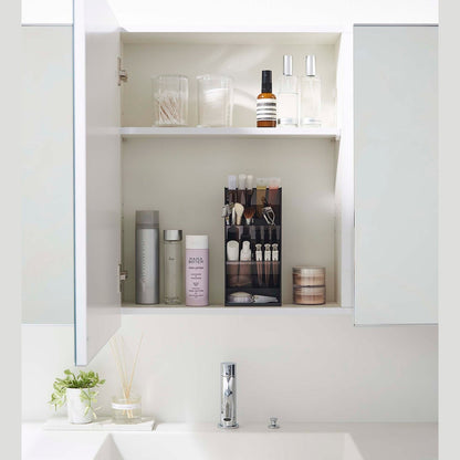 A front-facing view of an opened white medicine cabinet. Sunlight is focused on the right upper corner. The top half of the cabinet holds face serums and two clear containers with cotton swabs and rounds.