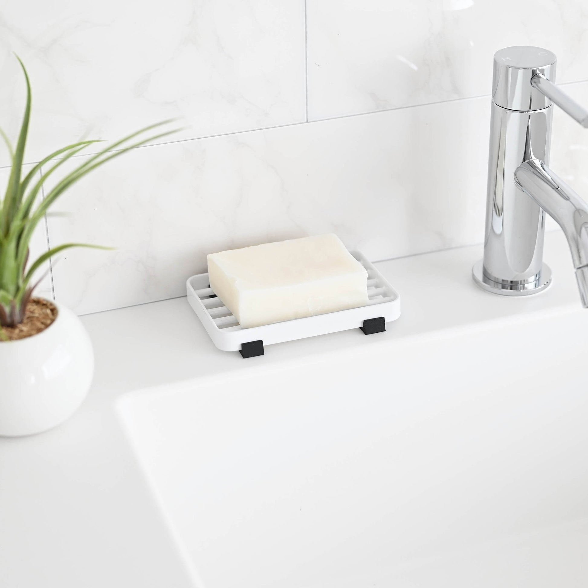 White Slotted Soap Tray holding soap bar on bathroom countertop by Yamazaki Home.