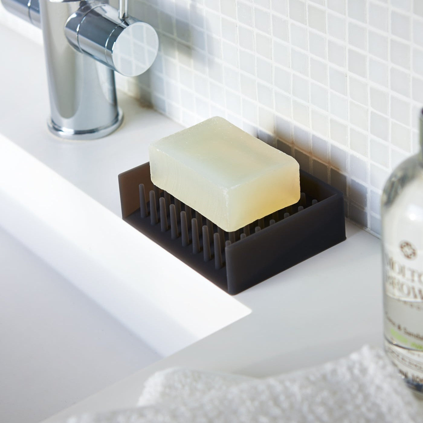 Black Self-Draining Soap Dish holding soap bar on sink counter by Yamazaki Home.