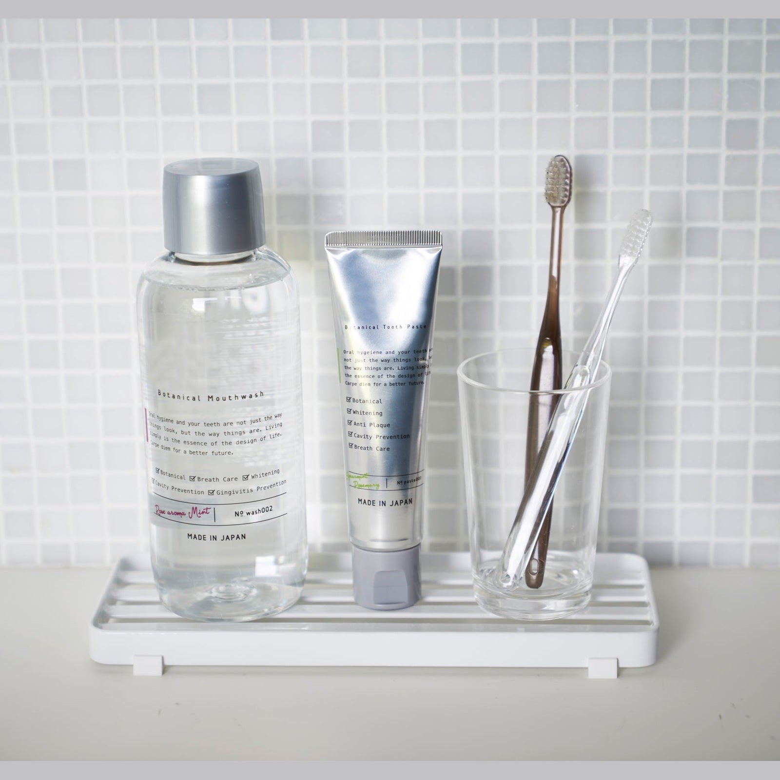 Front view of white Slotted Tray holding toothbrush, toothpaste, and mouthwash on bathroom sink by Yamazaki Home.