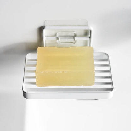 Yamazaki Home's black Traceless Adhesive Soap Tray mounted on a white wall, holding a bar of yellow soap, showcasing minimal design.