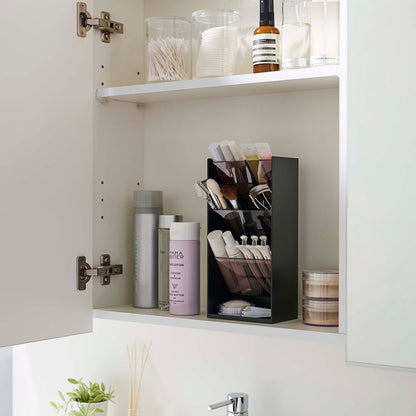 An angled view of an opened white medicine cabinet. Sunlight is focused on the right upper corner. The top half of the cabinet holds face serums and two clear containers with cotton swabs and rounds.