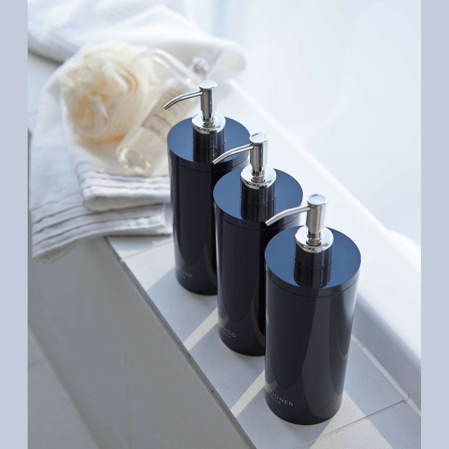Aerial view of black Body Soap Dispenser on bathtub edge by Yamazaki Home.