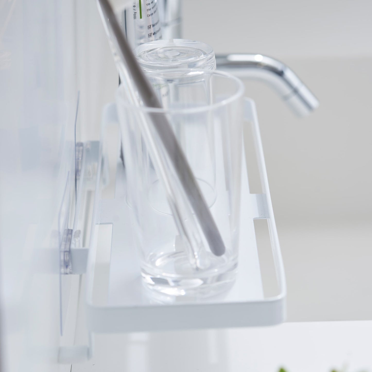 Side view of Yamazaki Home Traceless Adhesive Floating Tray with a glass and toothpaste resting on it