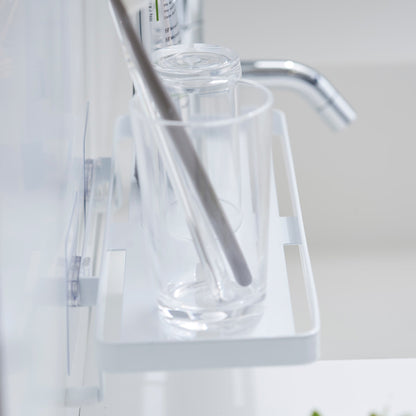 Side view of Yamazaki Home Traceless Adhesive Floating Tray with a glass and toothpaste resting on it