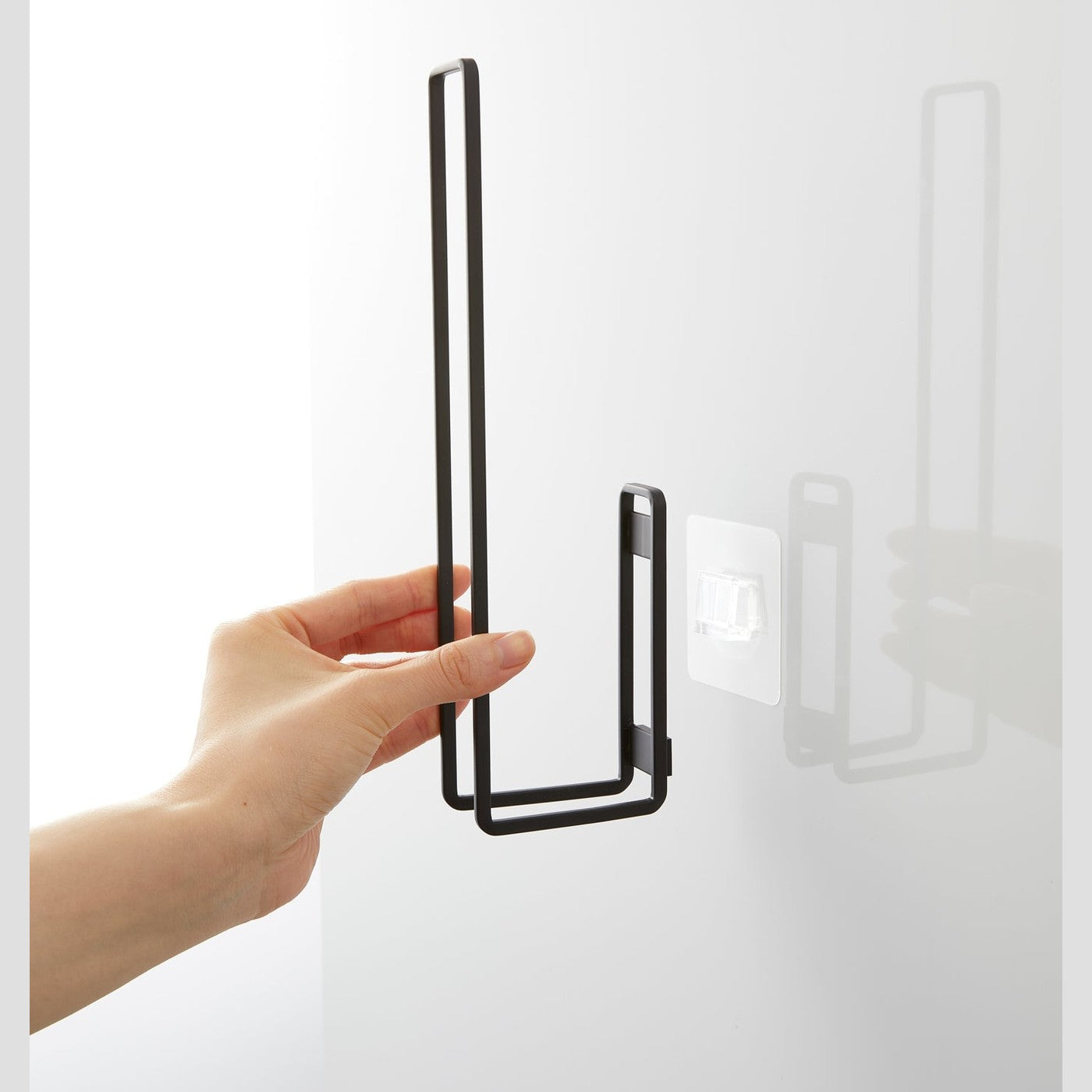 Attaching a black Yamazaki Home Traceless Adhesive Toilet Paper Holder to the adhesive hook