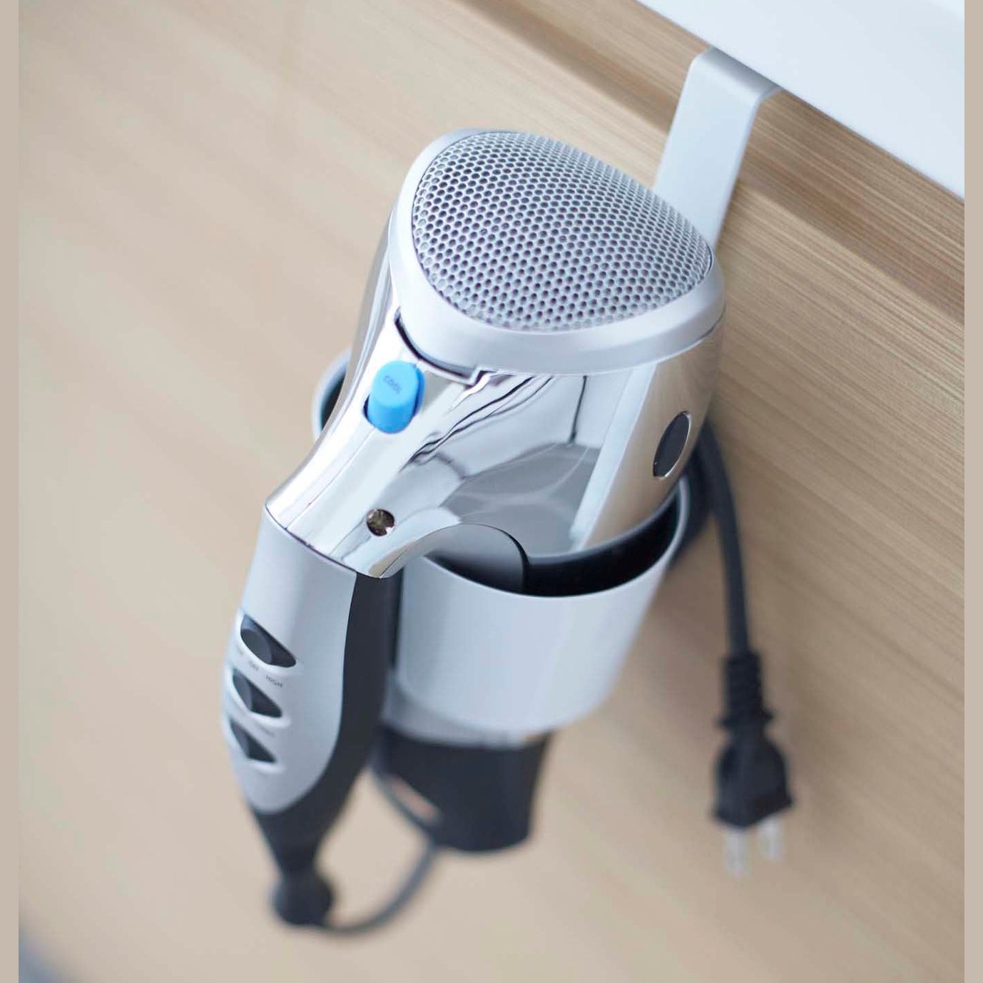 Close up view of white Blow Dryer Holder holding blow dryer on bathroom cabinet by Yamazaki Home.