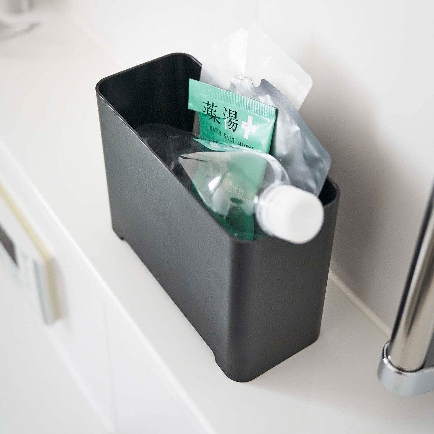 Top-down view of black Yamazaki Self-Draining Bathroom Organizer filled with bath supplies
