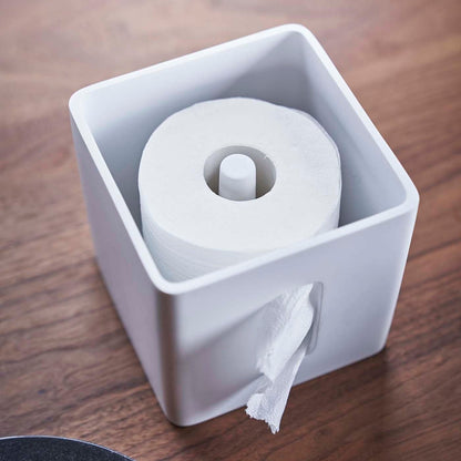 Aerial view of white toilet paper holder with cover off and holding toilet paper roll by Yamazaki Home.
